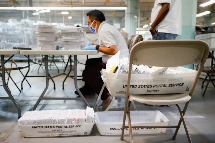 In New York a Board of Elections worker wearing a protective mask counts ballots from USPS bins in a secured facility.